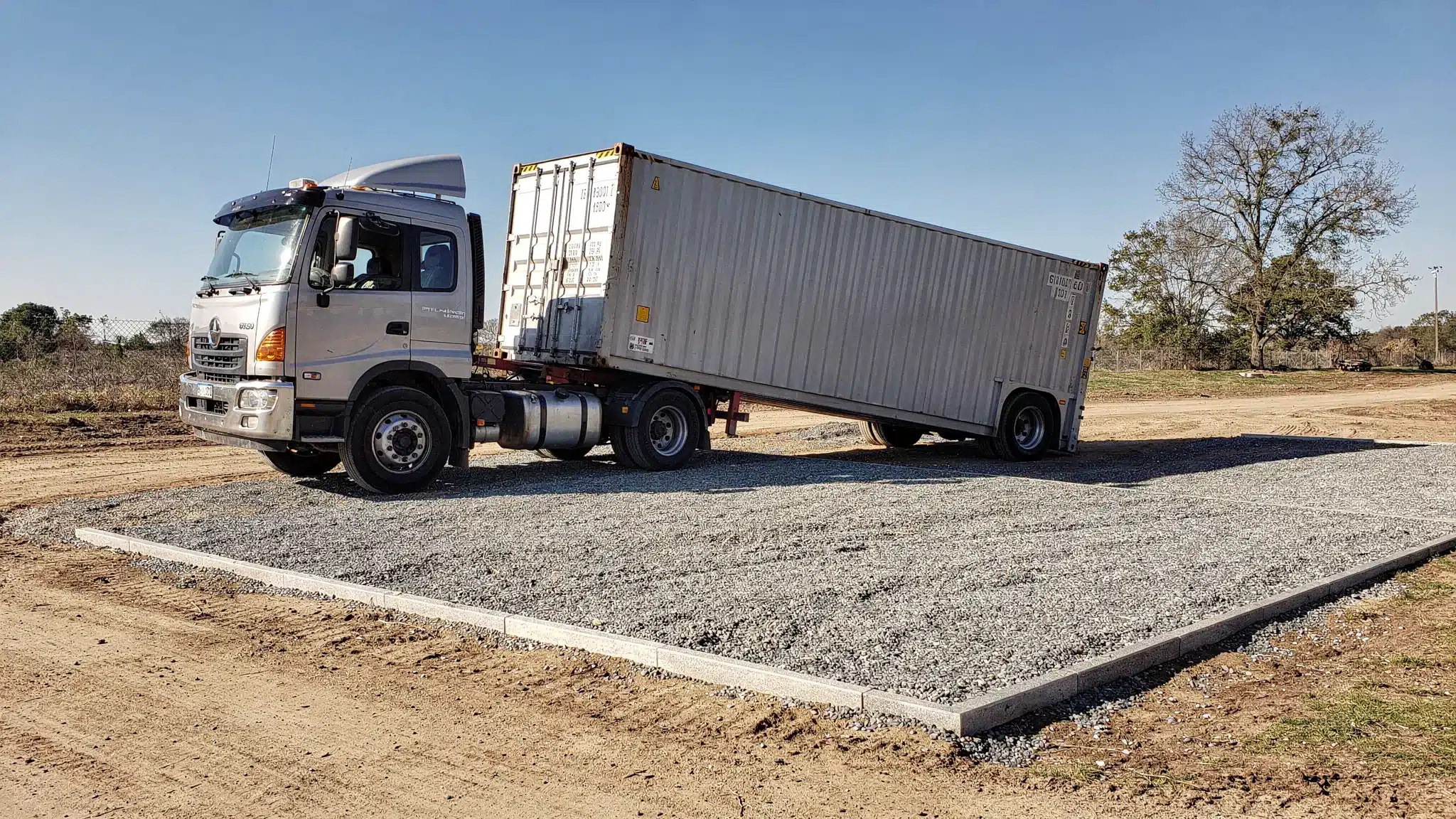 Storage Container Prices: What Impacts Your Delivered Quote 2 A tilt-bed truck delivering a shipping container to a prepared gravel pad with clear access, showing proper clearance and placement space.